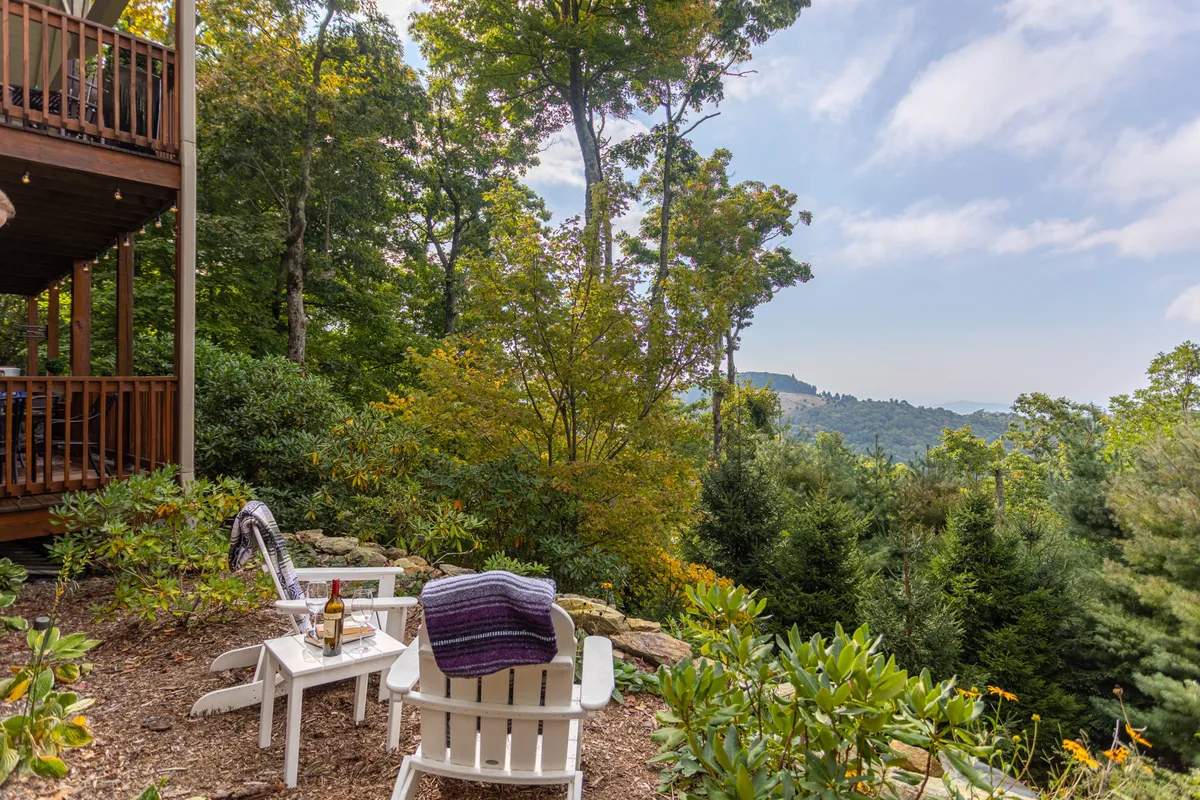 A pair of white Adirondack chairs overlook a vibrant autumn landscape with fiery foliage and distant mountain views. The setting suggests relaxation after a day of exploration and ties to the autumn and winter experiences mentioned in the text.