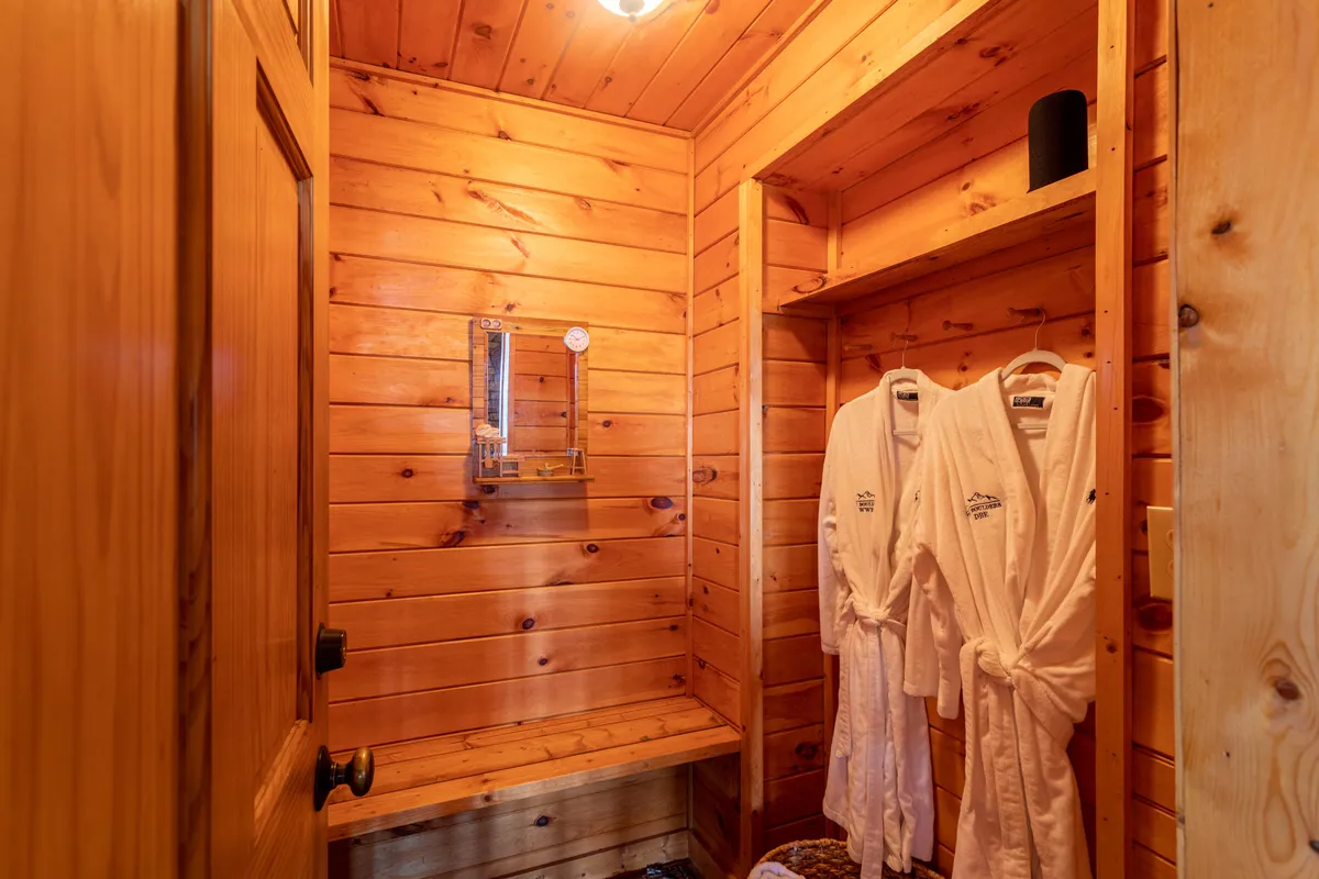 A spa-like bathroom with rich wooden paneling, a well-lit mirror, hanging bathrobes, and minimalist décor. The ambiance is calm and rejuvenating, evoking the feel of a personal spa retreat.
