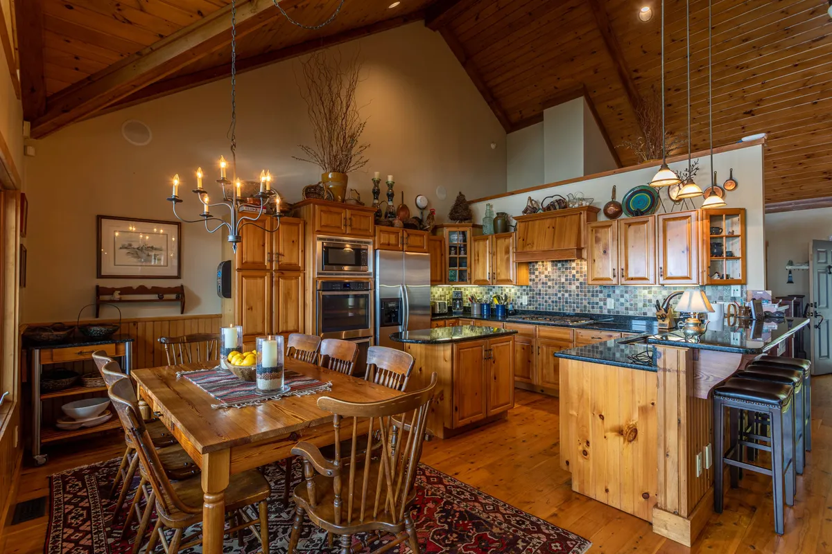A bright and open dining and kitchen area, featuring a large wooden dining table, gleaming granite countertops, and high-end stainless steel appliances. A chandelier provides warm lighting, while open shelving and decorative elements add a homely touch. The setting invites family meals, celebrations, and culinary creativity.