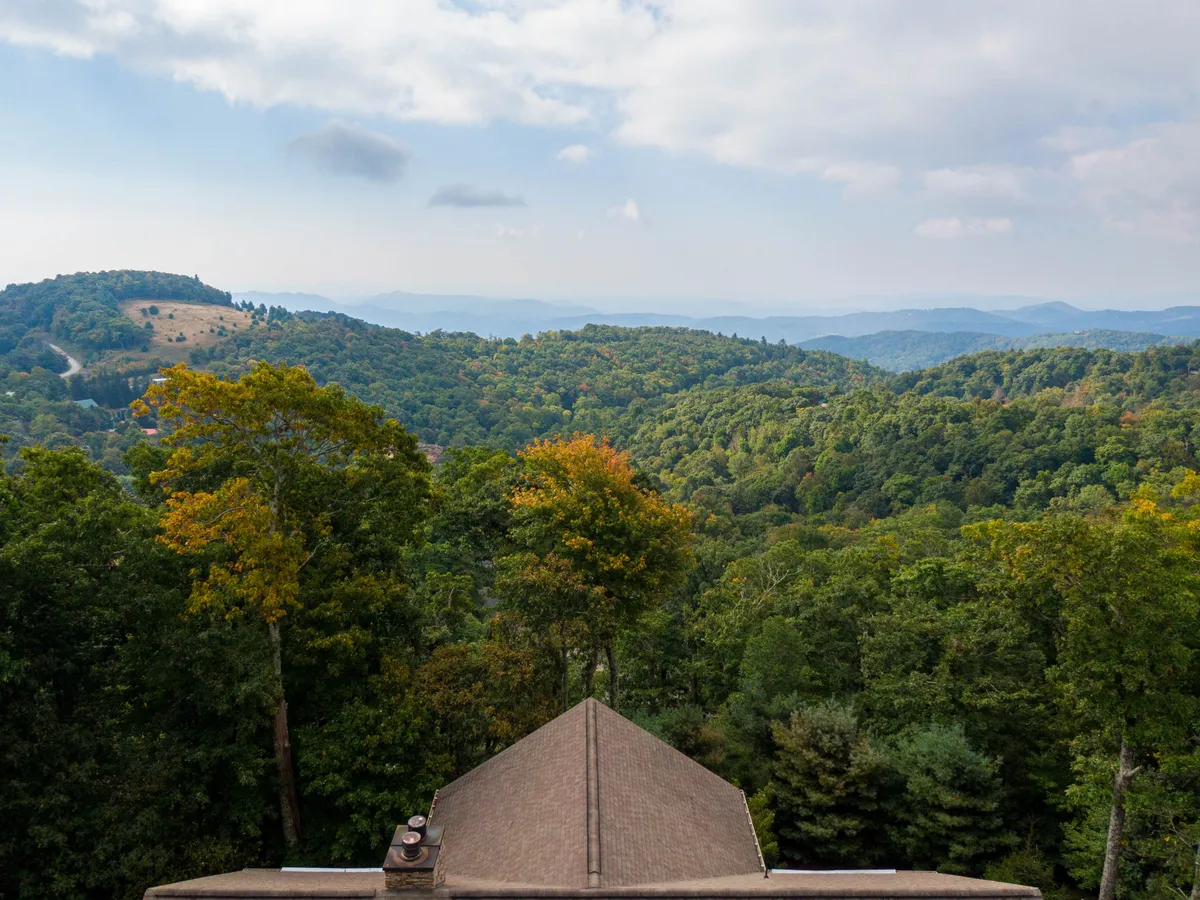 A stunning panoramic view of a mountain range enveloped by lush green trees under a serene sky dotted with clouds. The landscape embodies the natural beauty of the High Country and evokes the sense of endless outdoor adventure available year-round.