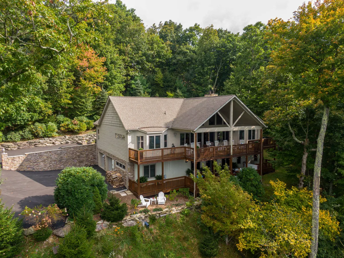 A spacious wooden deck nestled among mature trees, with a stone pathway leading into the surrounding wooded area. The deck is ideal for relaxing or gathering after a day outdoors, and the natural setting hints at easy access to hiking trails and pet-friendly adventures.