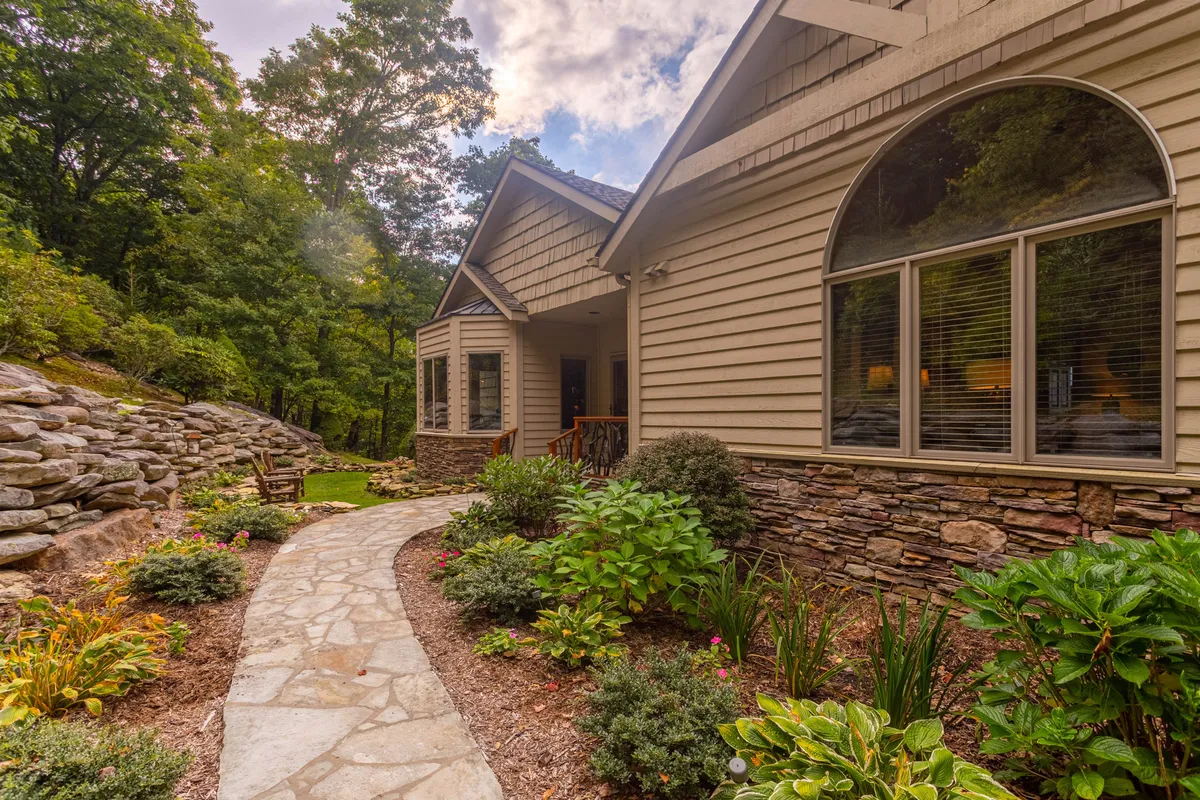 The exterior of the home featuring a stone pathway, lush greenery, large windows, and spaces for outdoor seating and gathering. The inviting scene is perfect for strolling, socializing, or enjoying the garden, reflecting both the privacy and communal aspects of the property.