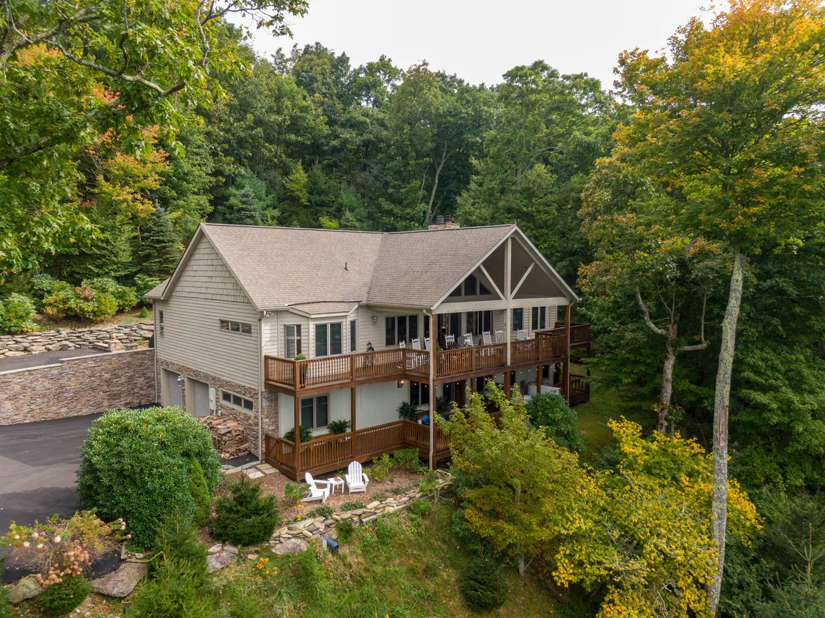 A large wooden deck nestled among lush greenery, featuring comfortable outdoor seating and a stone pathway leading to the surrounding landscaped yard. The space is expansive, inviting, and perfect for relaxation or gatherings, with plenty of room to enjoy nature and the mountain air.