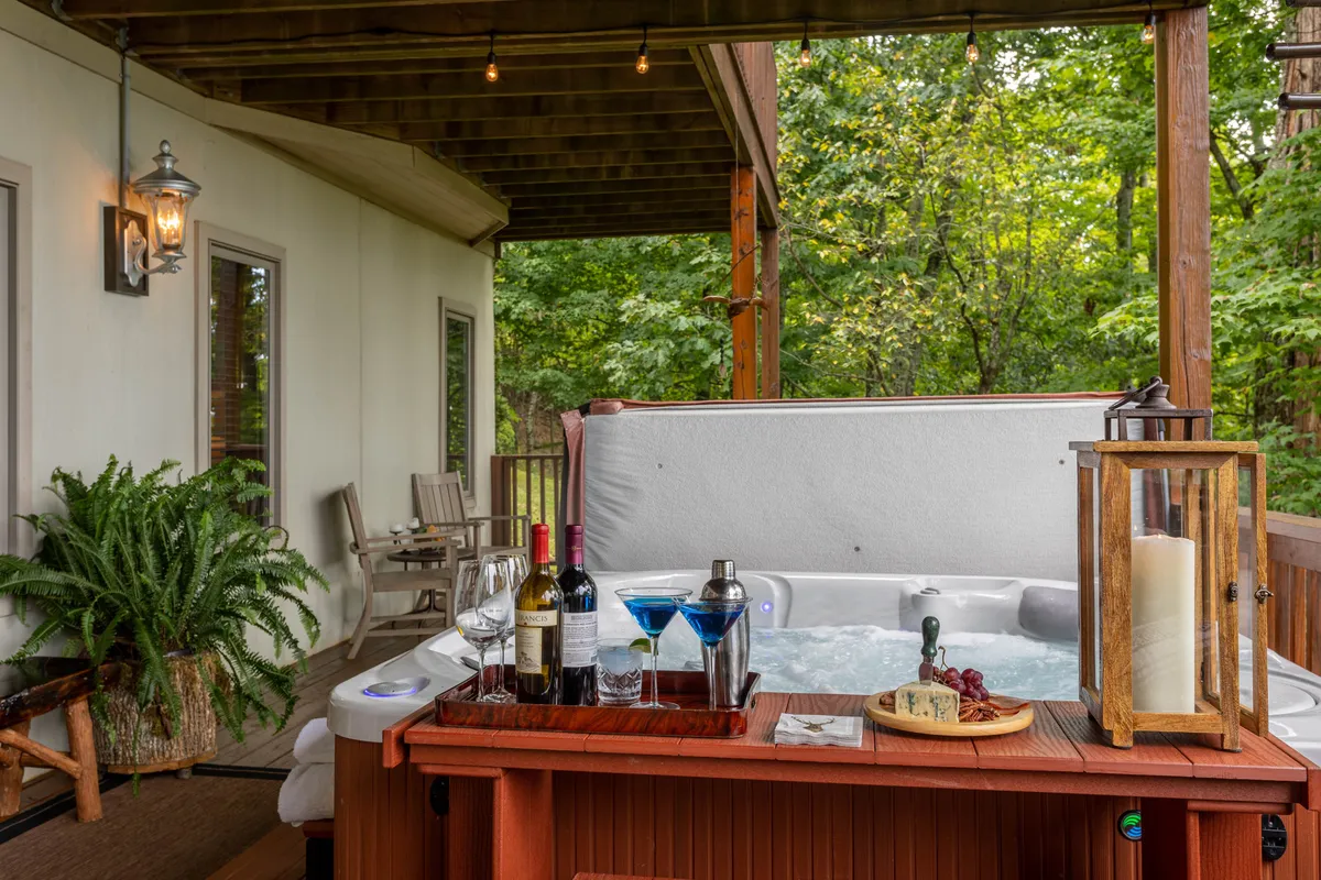 This exterior image showcases a luxurious outdoor hot tub area surrounded by lush greenery, complete with a beverage station and comfortable outdoor seating. The scene suggests a social and tranquil atmosphere—perfect for unwinding after a day of adventure, sharing drinks with friends, and soaking in the natural beauty.