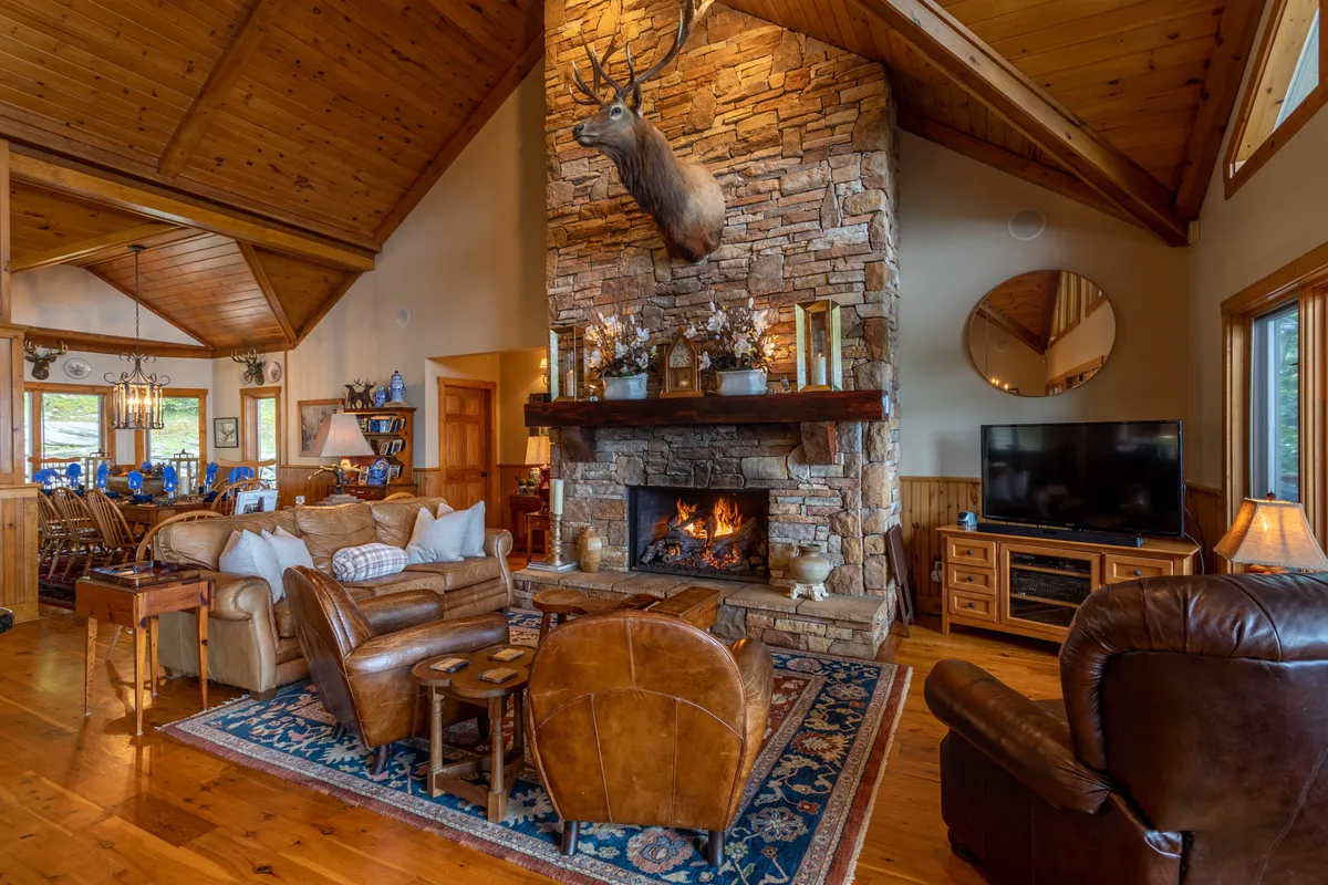 A welcoming interior scene highlighting a spacious living and dining area. The stone fireplace and mounted deer head anchor the room, while a comfortable seating arrangement and wooden dining space invite both relaxation and communal dining. Warm lighting and rustic decor create a setting ideal for family gatherings and special occasions.