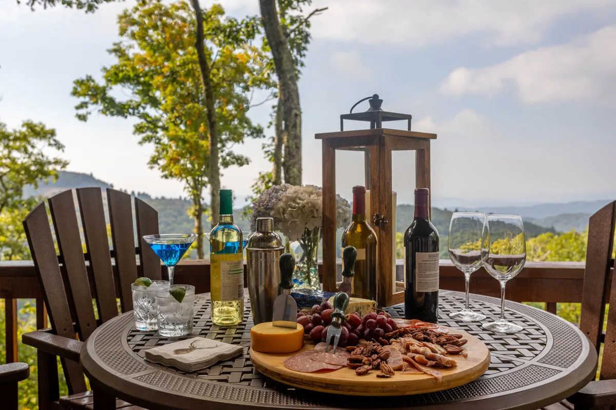 A charcuterie board and bottles of wine are set atop a wooden outdoor table overlooking a scenic vista, inviting social gatherings and relaxation. The atmosphere is warm and sociable, capturing the essence of outdoor dining and memory-making.
